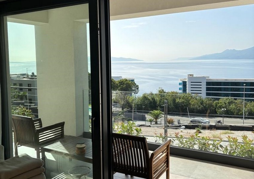 Balkong med trästolar och havsutsikt genom en öppen glasdörr, fastighetsnotering i Rijeka, Kroatien.