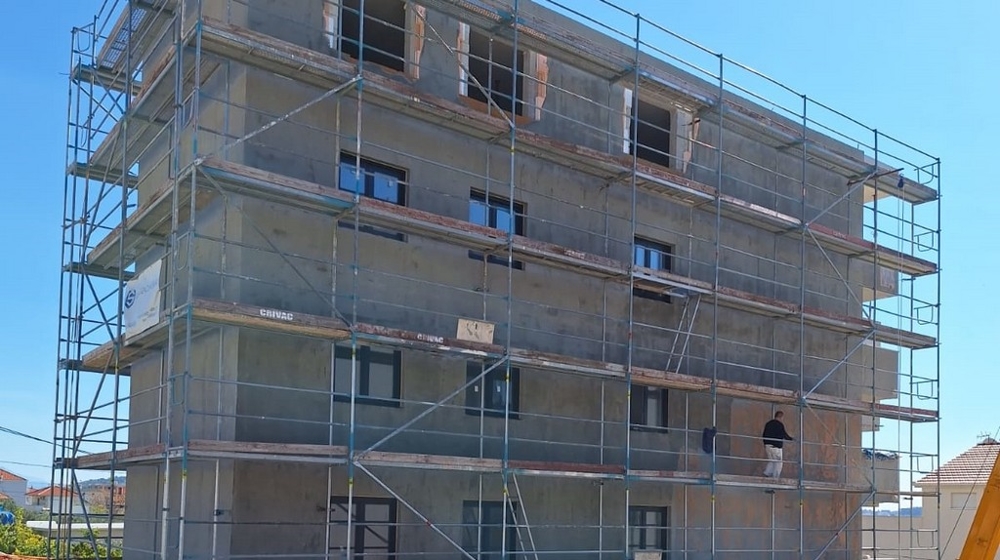Hyreshus i byggskede med byggnadsställningar, synligt skal, samt arbeten på det yttre murverket, blå himmel i bakgrunden.