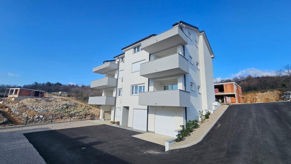 Exteriör vy av ett vitt hyreshus till salu i Crikvenica, Kroatien, med parkeringsplats och klarblå himmel