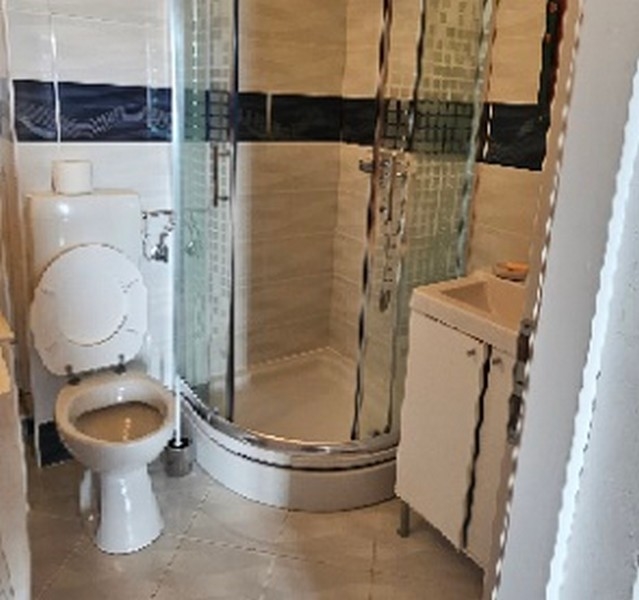 Badrum med svängd duschkabin, wc och handfat i kaklat rum