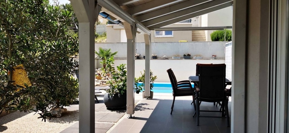 Täckt terrass med uteservering, del av lägenhet till salu i Tisno, Kroatien, med utsikt över poolen.