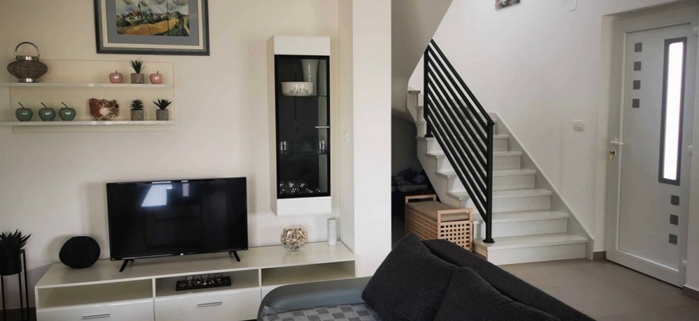 Interiörvy av vardagsrummet på bottenvåningen av lägenheten till salu i Tisno, Kroatien, med TV och trappor.