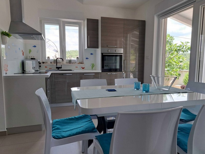 Modernt kök med vita möbler och matplats i lägenhet till salu i Tisno, Kroatien.