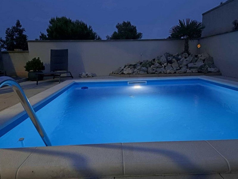 Kvällsvy över den upplysta utomhuspoolen i lägenheten till salu i Tisno, Kroatien.