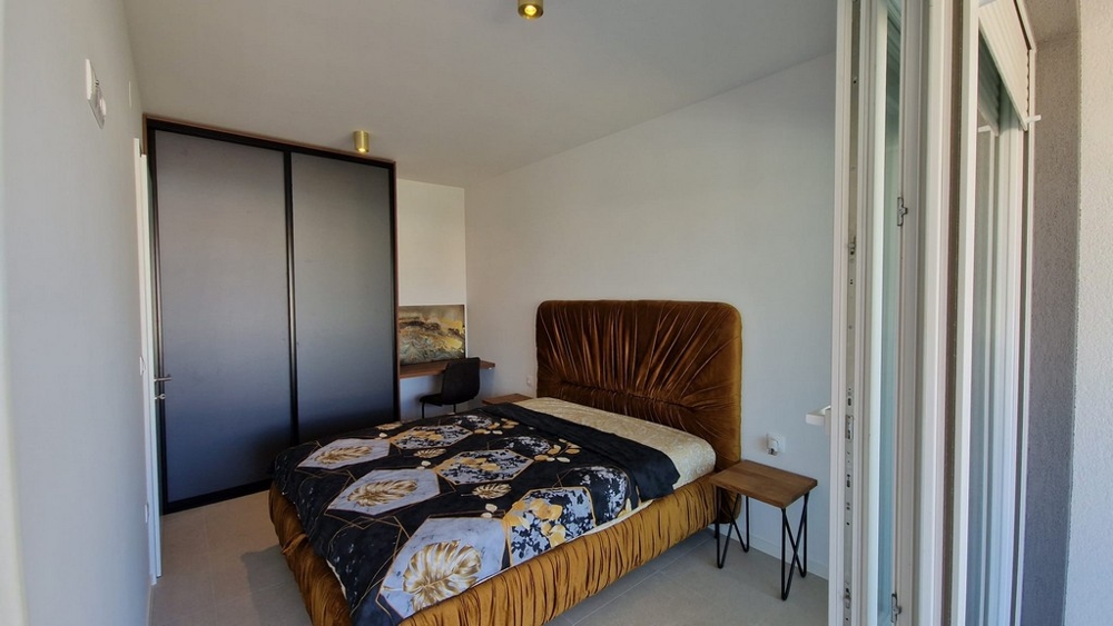 Sovrum i en lägenhet i Novalja, ön Pag, med en brun säng och tillgång till en balkong, fastigheter Kroatien