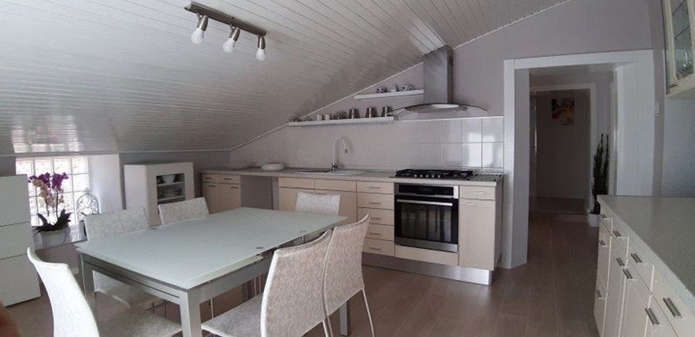 Ett modernt ljust kök med vit inredning och matplats under snedtak