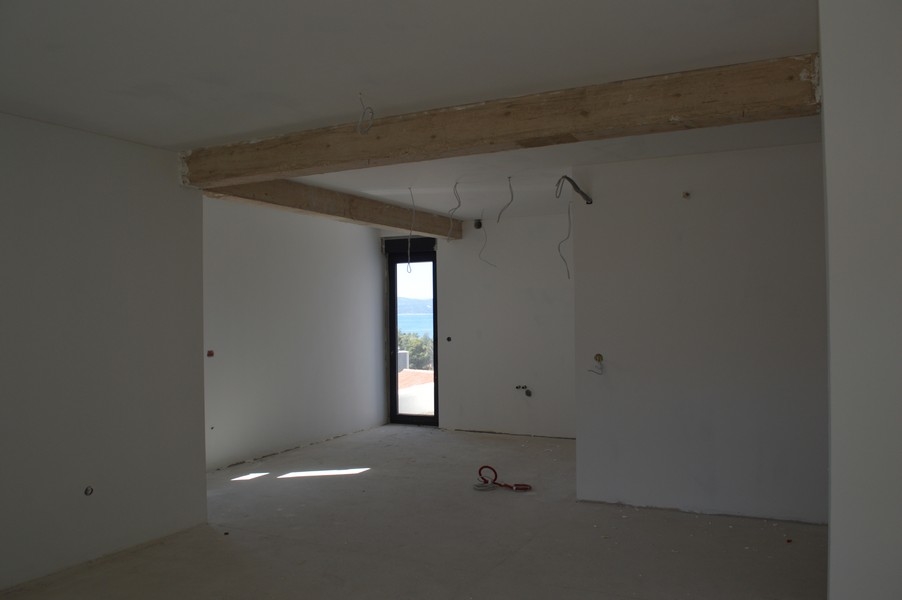 Rymligt vardagsrum i en oavslutad lägenhet med synliga takbjälkar och havsutsikt.