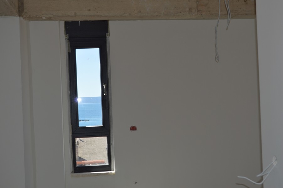 Smalt fönster i en oavslutad lägenhet med havsutsikt.