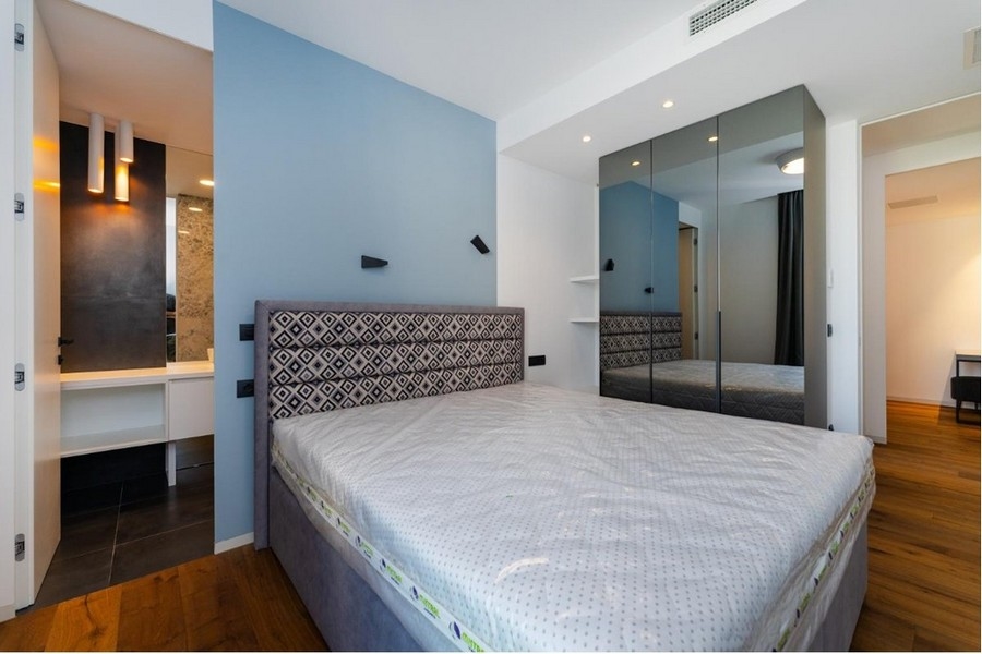 Sovrum med blåvita väggar, grå säng, spegelskåp