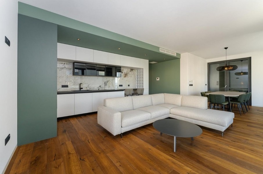 Öppet vardagsrum med kök, trägolv, grön vägg
