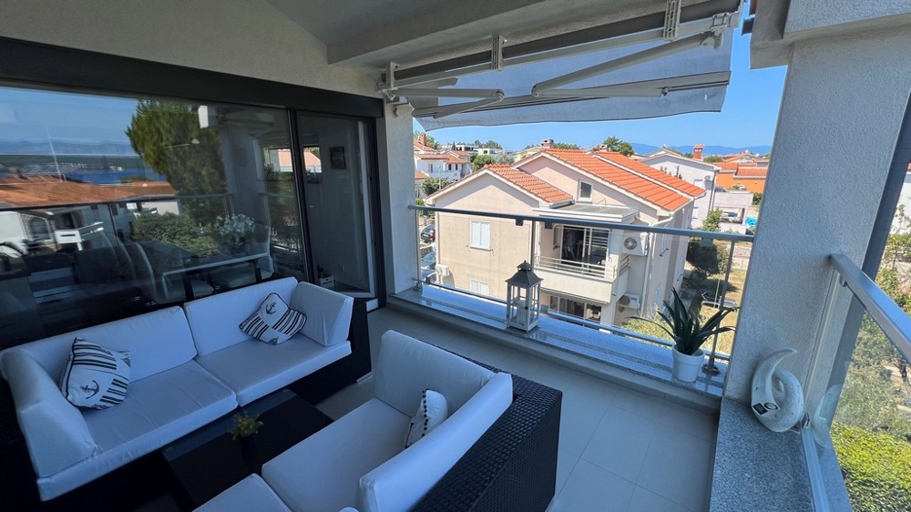 Terrass med utsikt över havet och närliggande hus, möblerad med vita soffor och maritima kuddar.