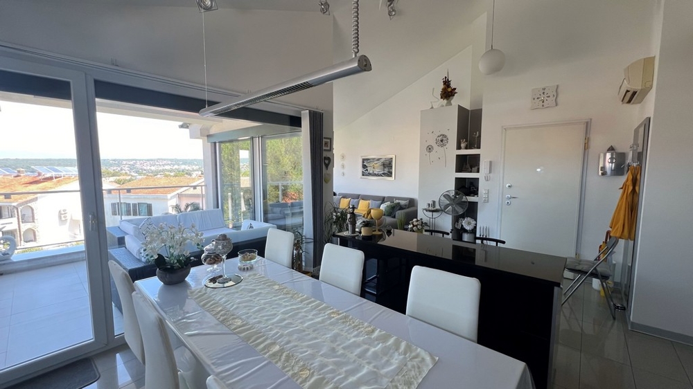 Matplats och kök med moderna möbler, stort fönster mot terrassen med havsutsikt.