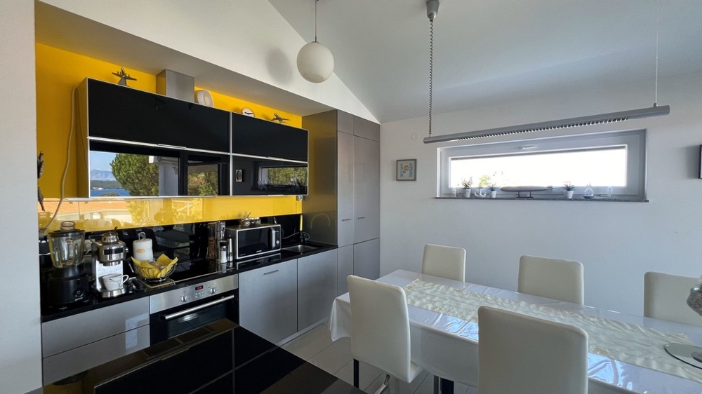 Modernt kök med svart bänkskiva och gul bakvägg, intilliggande matplats.