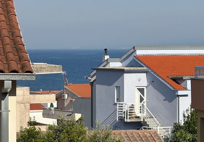 Utsikt över ett bostadsområde med ett hus med ett rött tegeltak med utsikt över det blå havet och den avlägsna kustlinjen