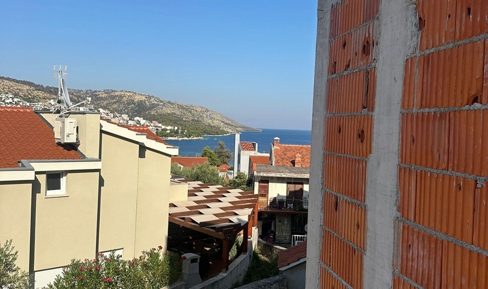 Delvis färdig byggnad med exponerat tegel, med utsikt över en stadsdel med röda tegeltak och havet i bakgrunden