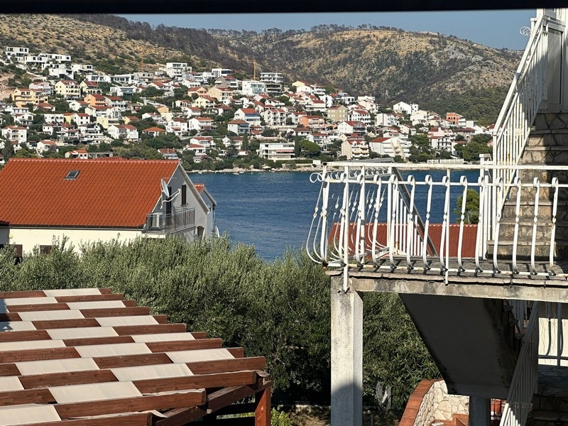 Vacker utsikt över en kuststad med hus med röda tak, grön vegetation och kullar i bakgrunden över bukten