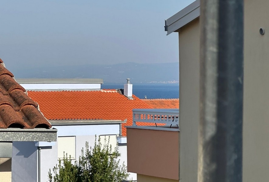 Närbild av röda tegeltak med en liten glimt av havet i fjärran