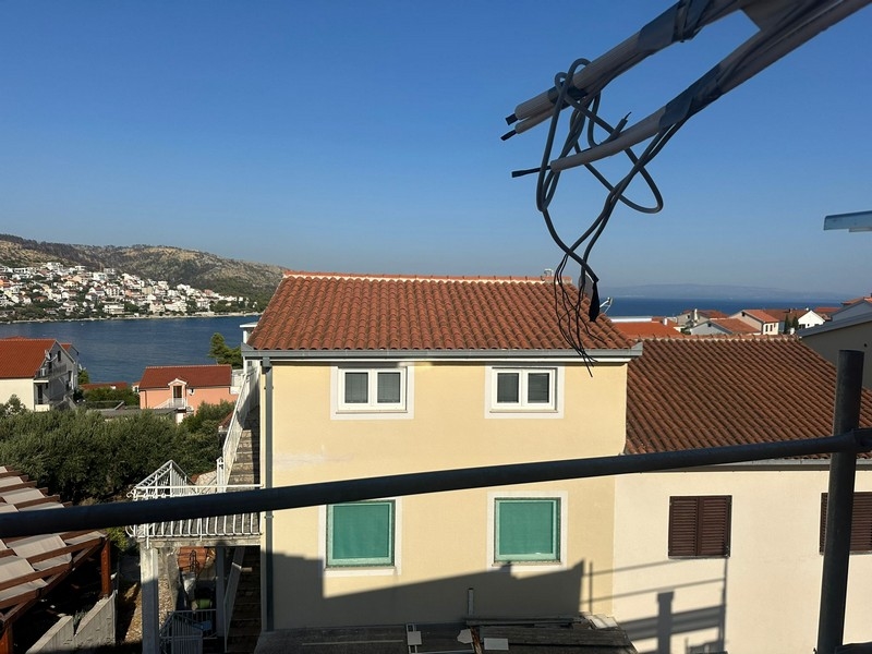 Panoramautsikt från en balkong under uppbyggnad, med utsikt över närliggande hus och kustlinjen som sträcker sig till horisonten