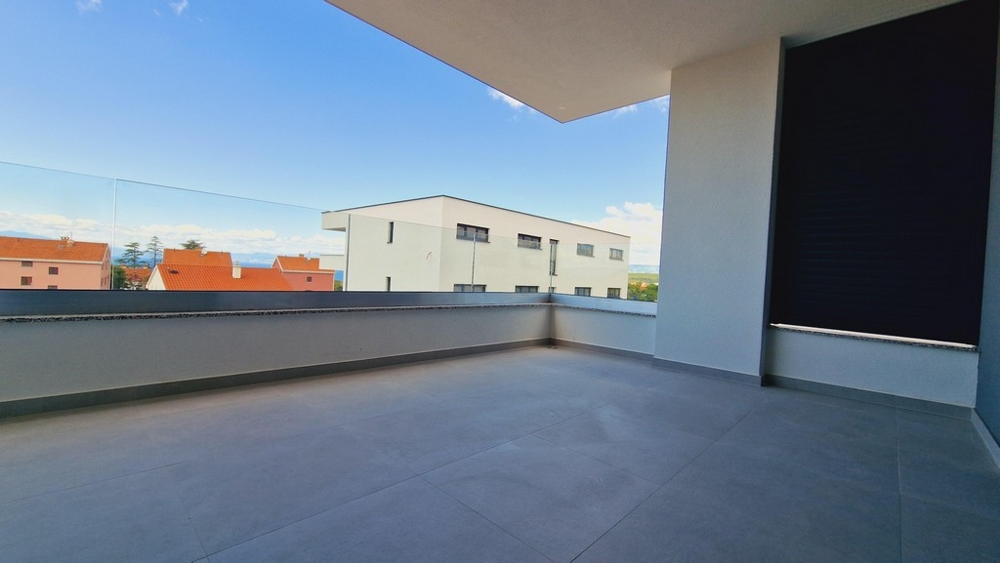 Rymlig terrass med glasräcken och utsikt över närliggande byggnader och horisonten