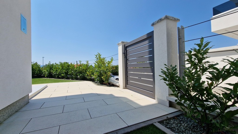 Entréport till modern byggnad med stenlagd förgård och gröna växter.