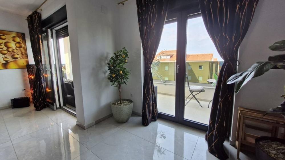 Vy över två balkongdörrar med gardiner, krukväxt i hörnet