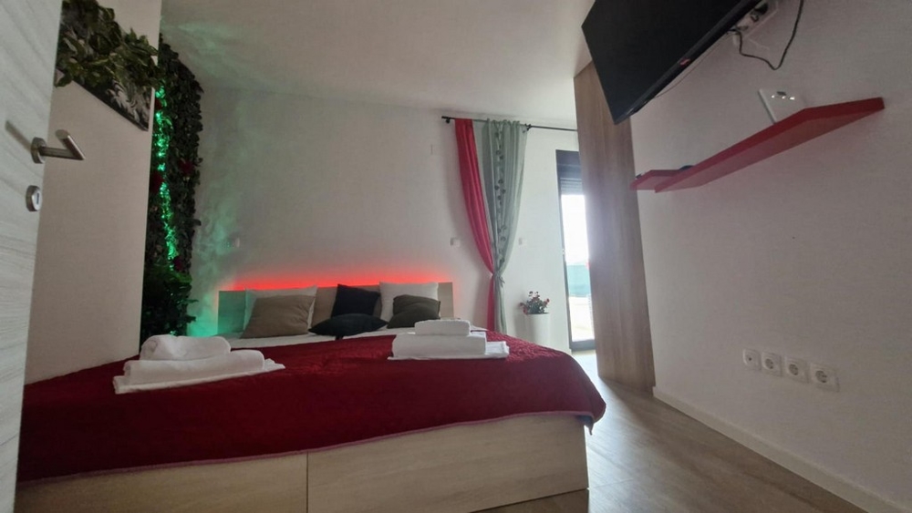 Sovrum med rött överkast, dekorativ bakgrund och TV på väggen