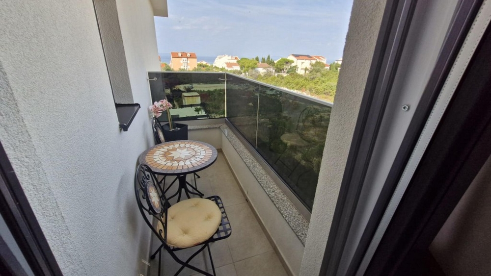 Balkong med litet bord och två stolar, utsikt över närliggande byggnader