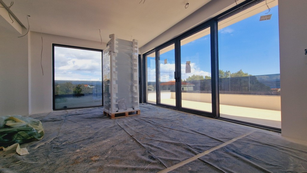 Interiörvy av den moderna nya lägenheten med stora fönsterfronter och utsikt över terrassen och havet.