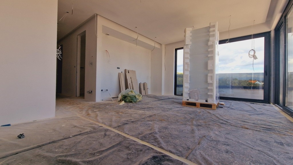 Bostadsdel i den nya byggnaden i färdigställandefasen, med utsikt över de stora glasfönstren och den omgivande naturen.