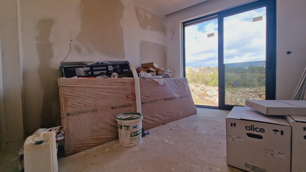 Oavslutat rum med byggplatsmaterial och ett stort fönster med utsikt över landskapet.