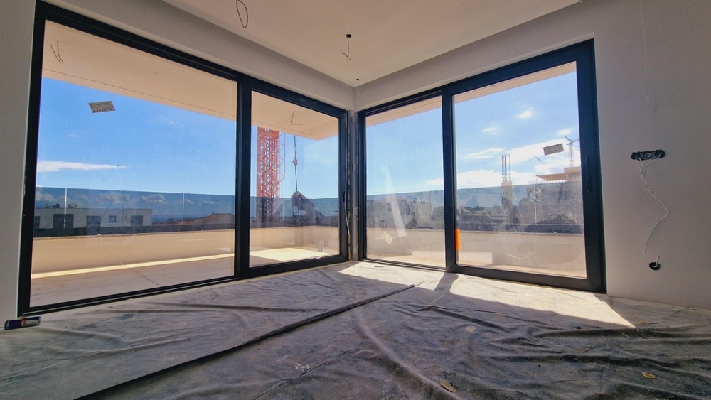 Vardagsrum med två stora glasfronter som släpper in mycket dagsljus och erbjuder utsikt över närområdet.