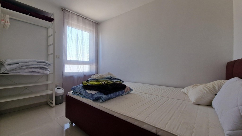 Sovrum med minimalistisk inredning, fönster och öppen klädförvaring.