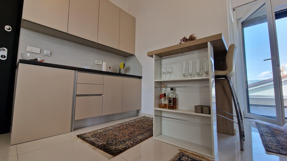 Litet modernt pentry med integrerade hyllor och barstolar, utgång till altan.