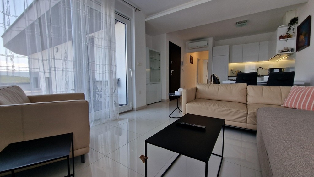 Öppen vardagsrumsdel med ljusa möbler, glasdörr till altan och integrerat pentry.