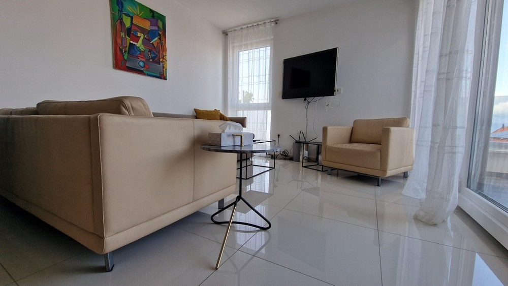 Stilrent inrett vardagsrum med soffa, tv och stora fönster som släpper in mycket ljus.