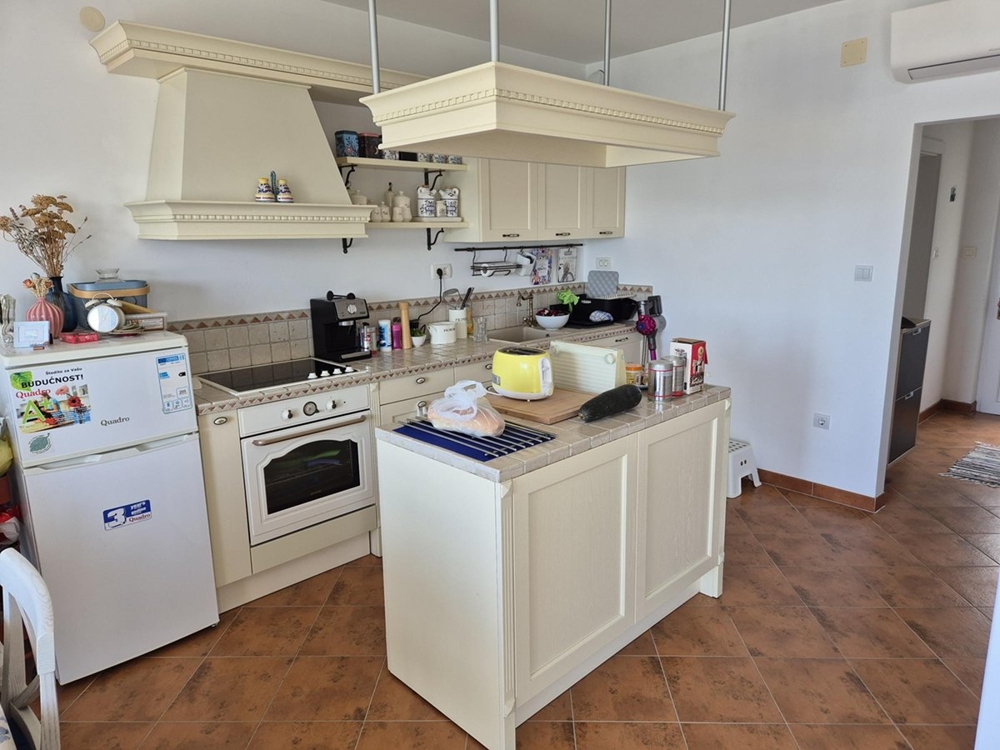 Ett ljust öppet kök med beiga skåp, en kokö och klinkergolv.