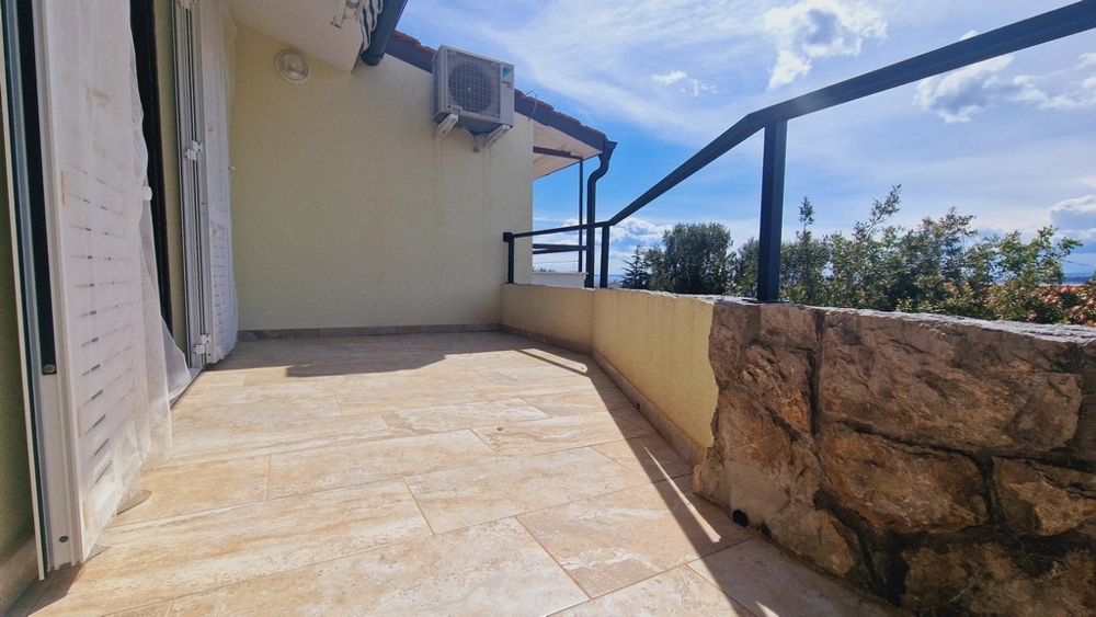 Solig terrass med stenmur och utsikt över den omgivande grönskan och himlen.