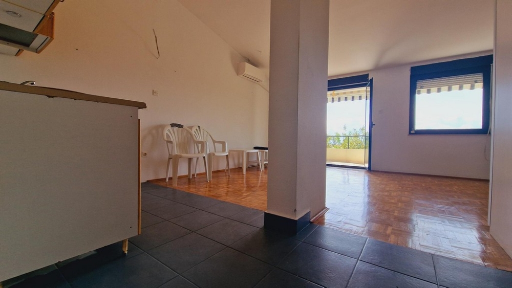 Vardagsrum med öppen övergång till kök, enkla vita möbler och klinkergolv.