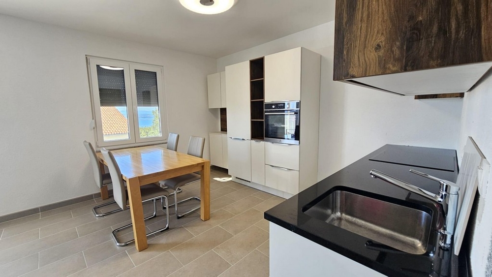 Ljust kök med matbord, moderna vitvaror och ett fönster med utsikt över havet.