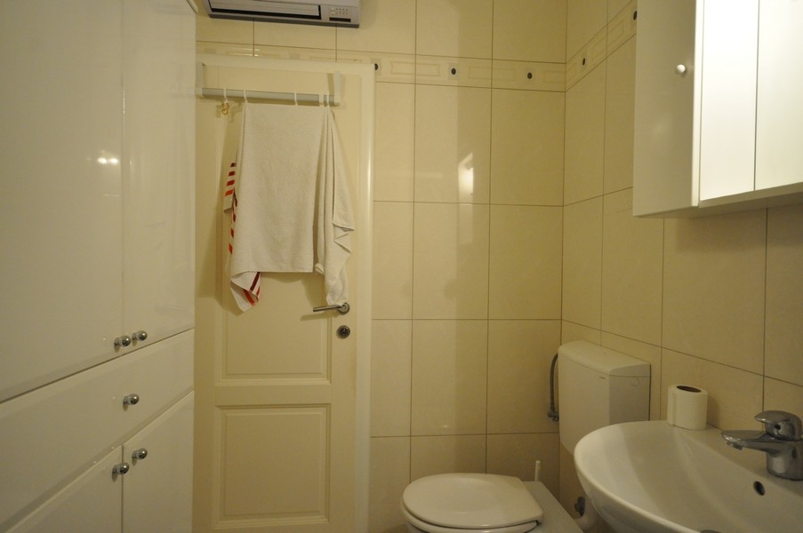 Badrum med wc, handfat, handdukshängare på dörren, ljust kakel, modern utrustning