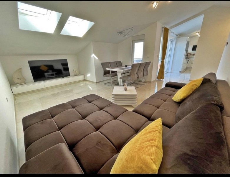 Modernt vardagsrum med takfönster, stor soffa, matbord och tv.