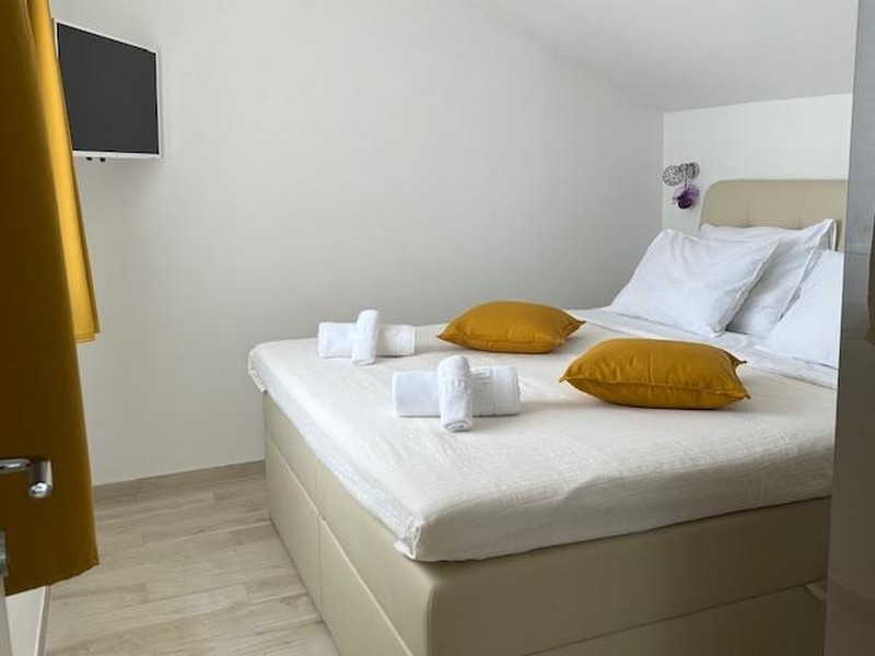 Sovrum med stor säng, gula kuddar och tv på väggen.