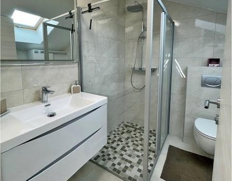 Modernt badrum med duschkabin och handfat.