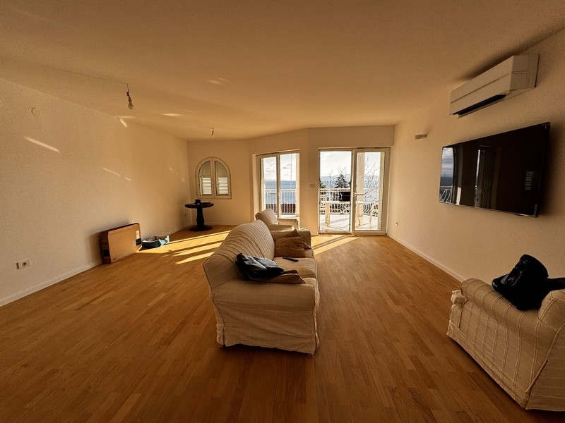 Ljust vardagsrum med vit soffa, vägghängd TV och panoramafönster mot havet