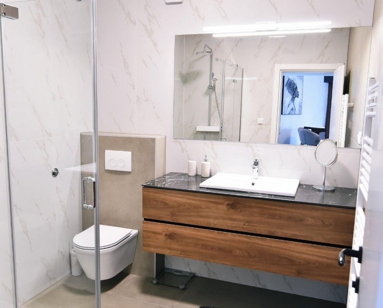 Modernt badrum med dusch, handfat och byrå i trä.