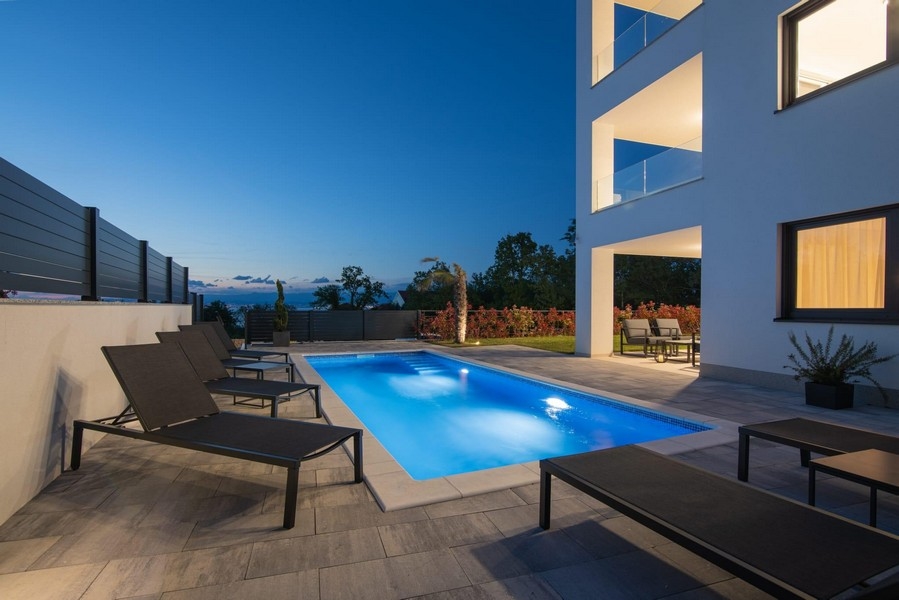 Nattbild av upplyst pool med solstolar