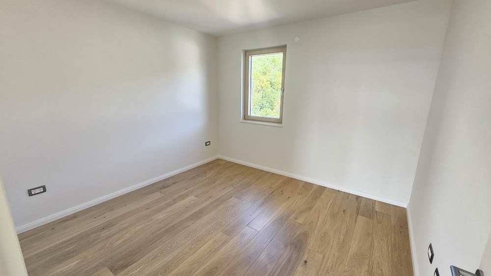 Ljust sovrum med trägolv och fönsterutsikt över grönskan