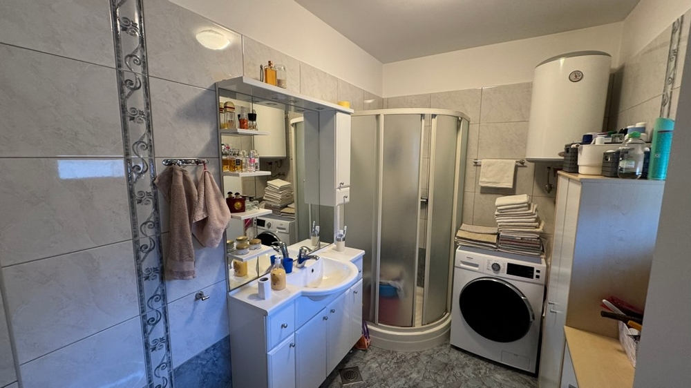 Badrum med dusch, tvättmaskin och handfat med spegel