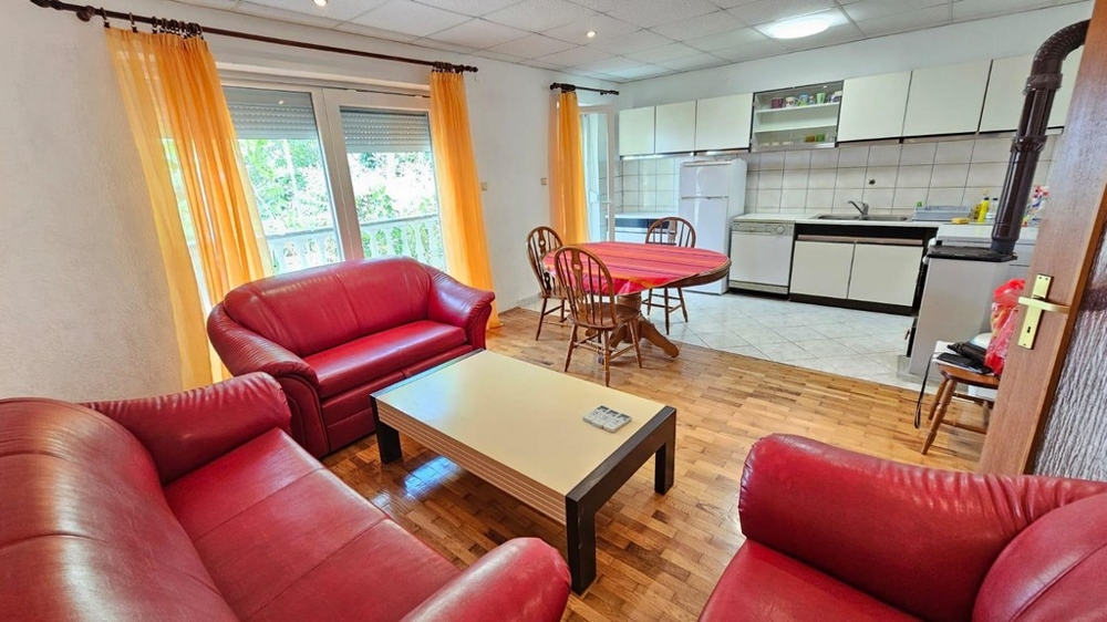 Vardagsrum med röd skinnsoffa, tillgång till balkong och öppet kök