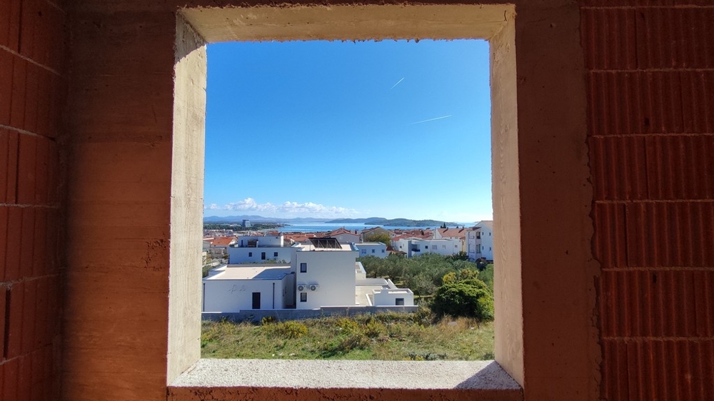 Utsikt genom oavslutade fönster över havet och bostadsområdet